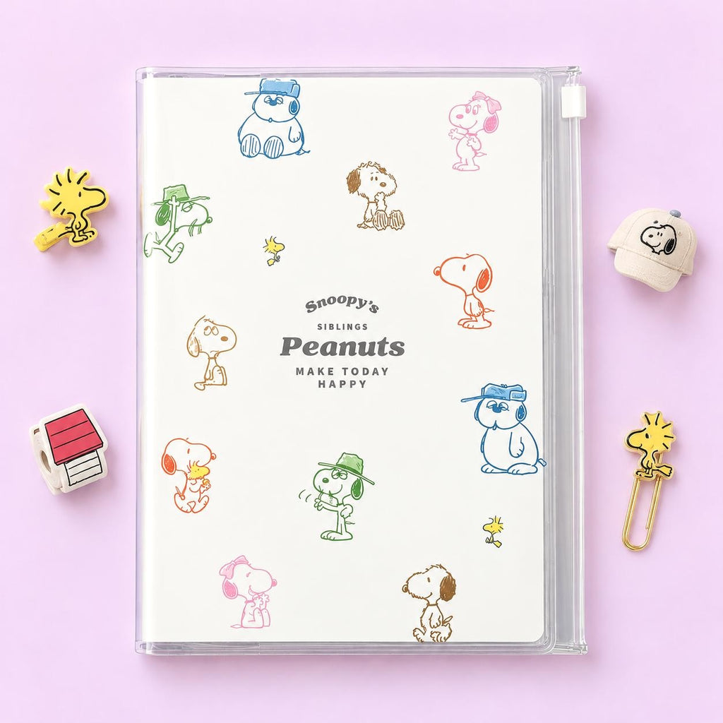 A Snoopy's Siblings Peanuts plastic organizer notebook with a clear cover, decorated with colorful cartoon character illustrations, displayed on a light pink background with themed props.
