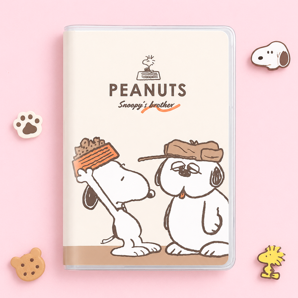 A hardcover 2027 notebook featuring the Peanuts 'Snoopy's Brother' design, displayed on a light pink background with small decorative character pins.