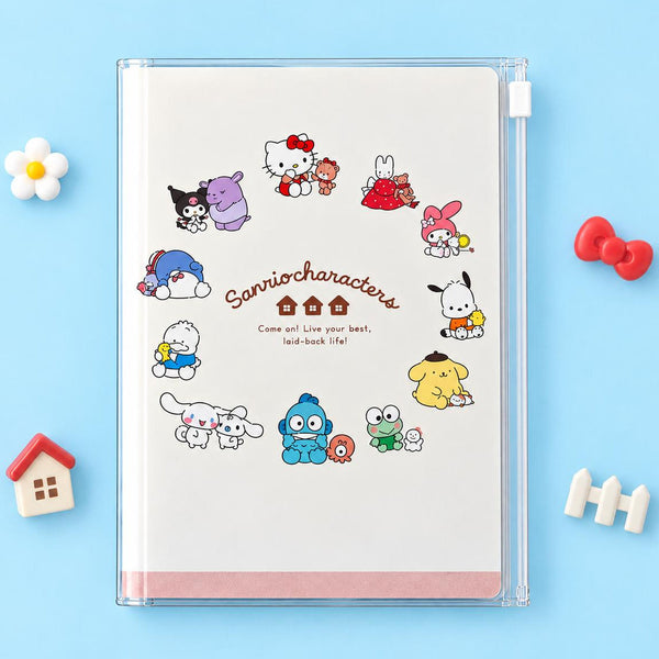 A 2027 Sanrio notebook case holding a white a circle of Sanrio characters printed around the center. The notebook is photographed on a light blue background with small decorative props around it.